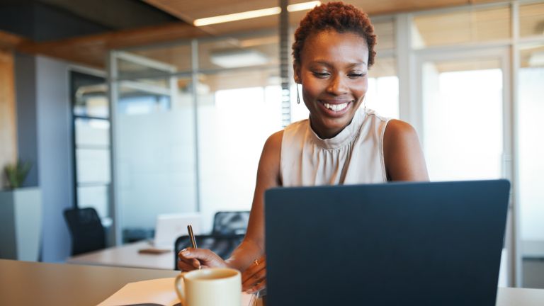 Woman working at a laptop while taking notes.