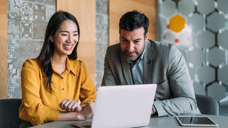 Two professional sitting at a desk working at a lap top